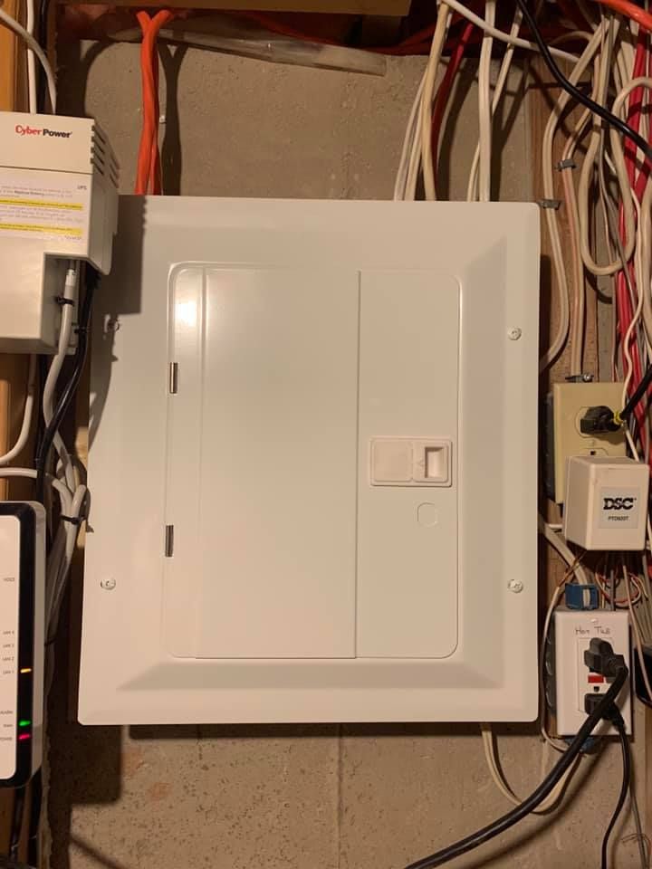 A white electrical box is hanging on a wall next to a bunch of wires.