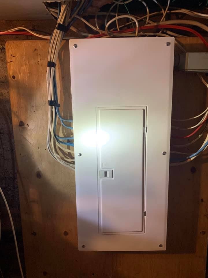 A white electrical box is hanging on a wooden wall.