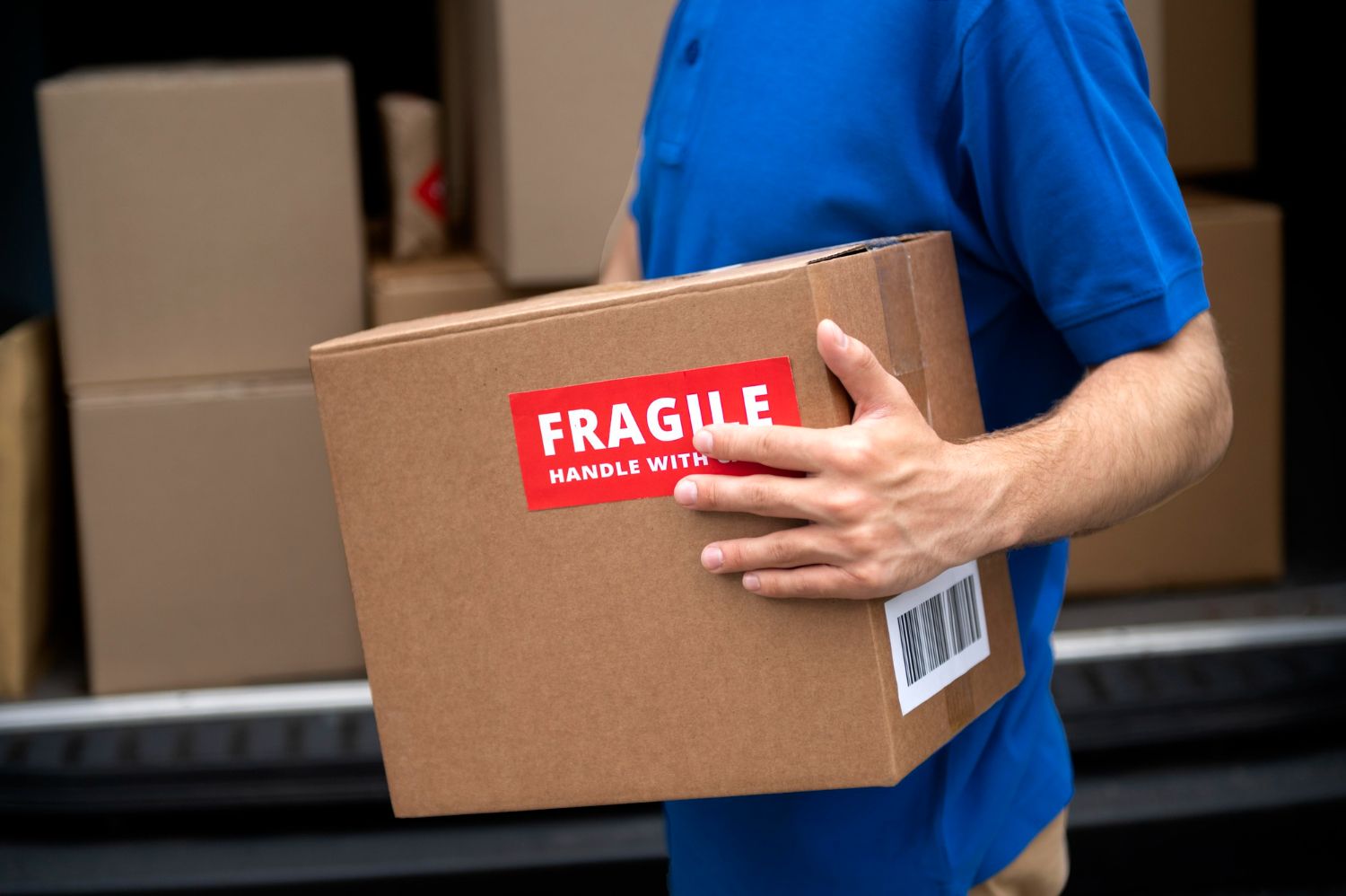 A delivery man is carrying a cardboard box with a fragile sticker on it.