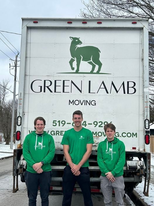 Three men are standing in front of a green lamb moving truck.