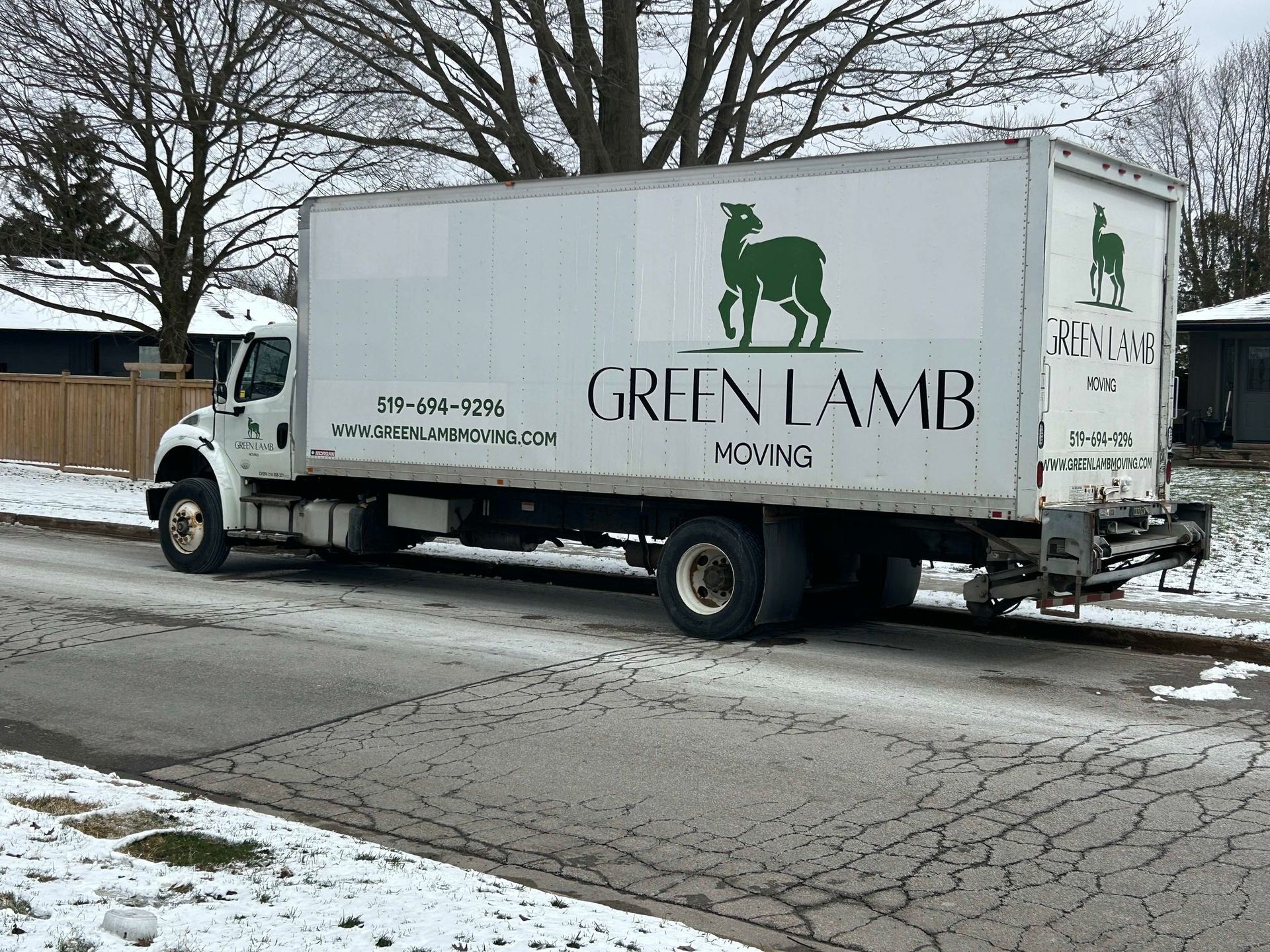 A green lamb moving truck is parked on the side of the road.