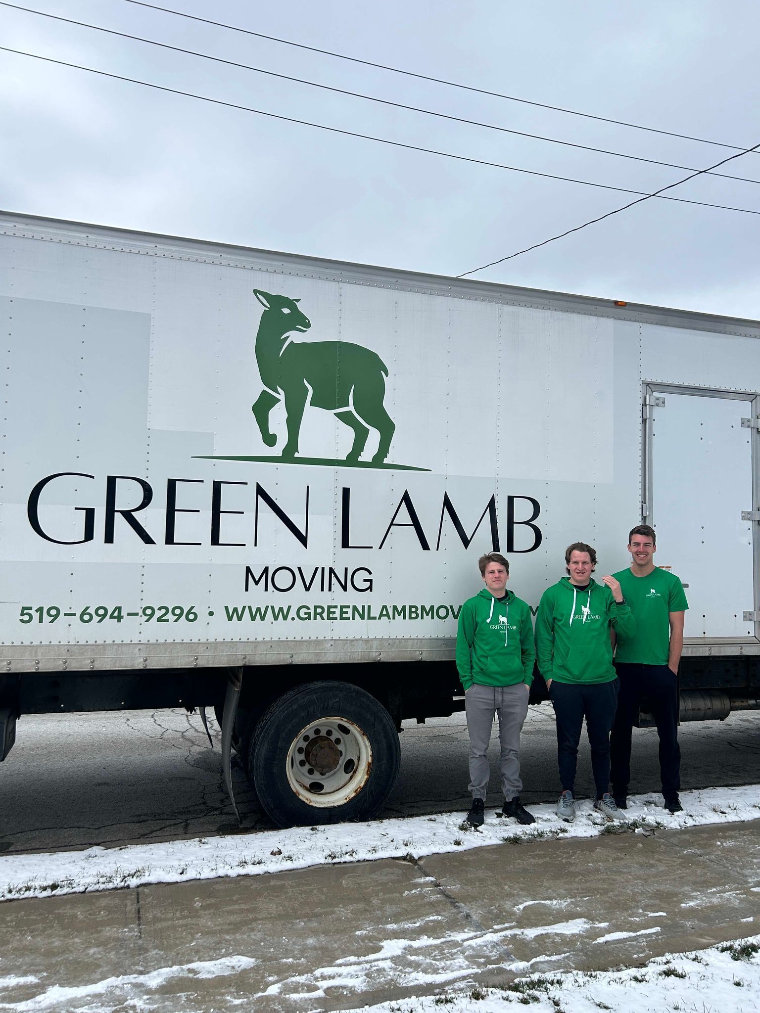 Three men are standing in front of a green lamb moving truck