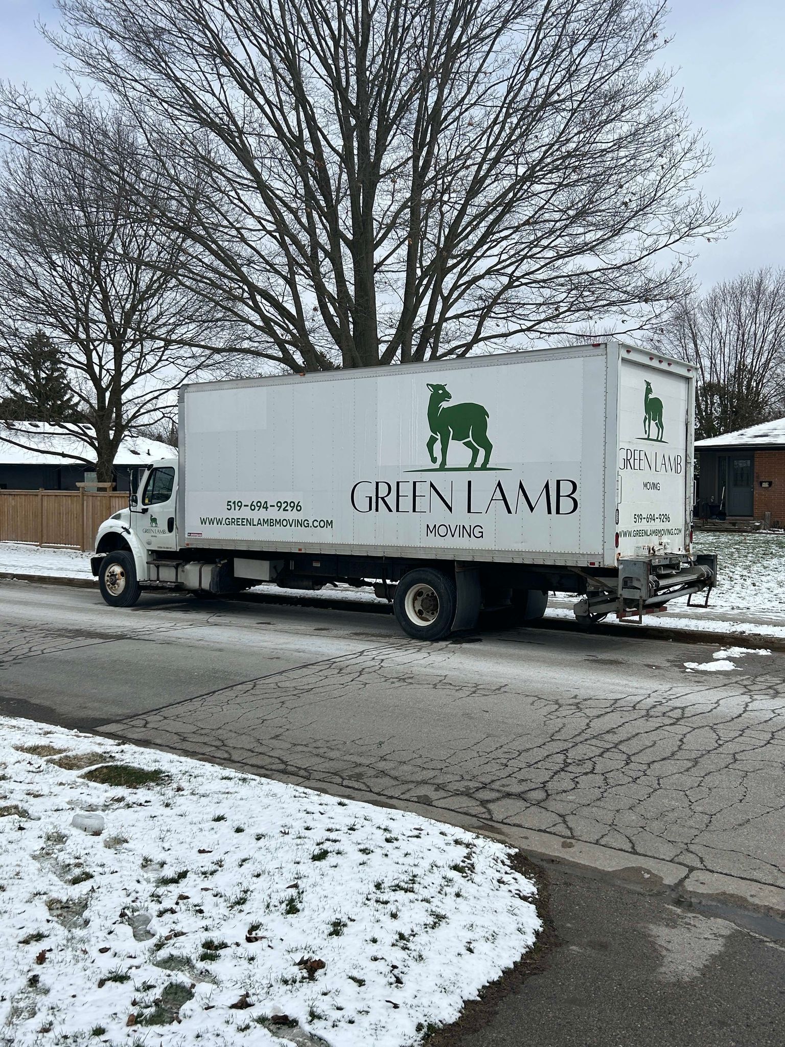 Two moving trucks are parked on the side of the road in the snow.