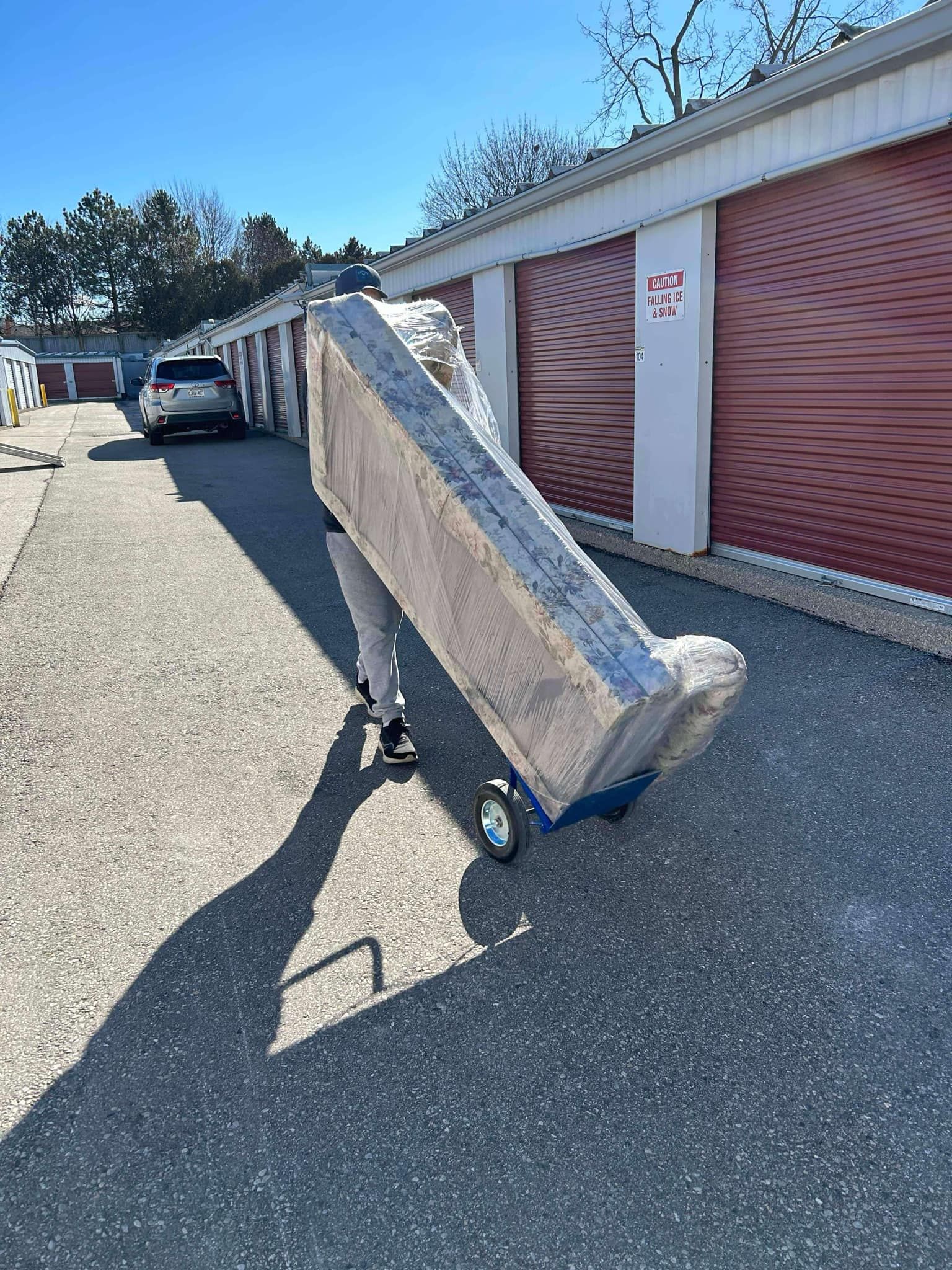 A person is pushing a mattress on a dolly in a parking lot.
