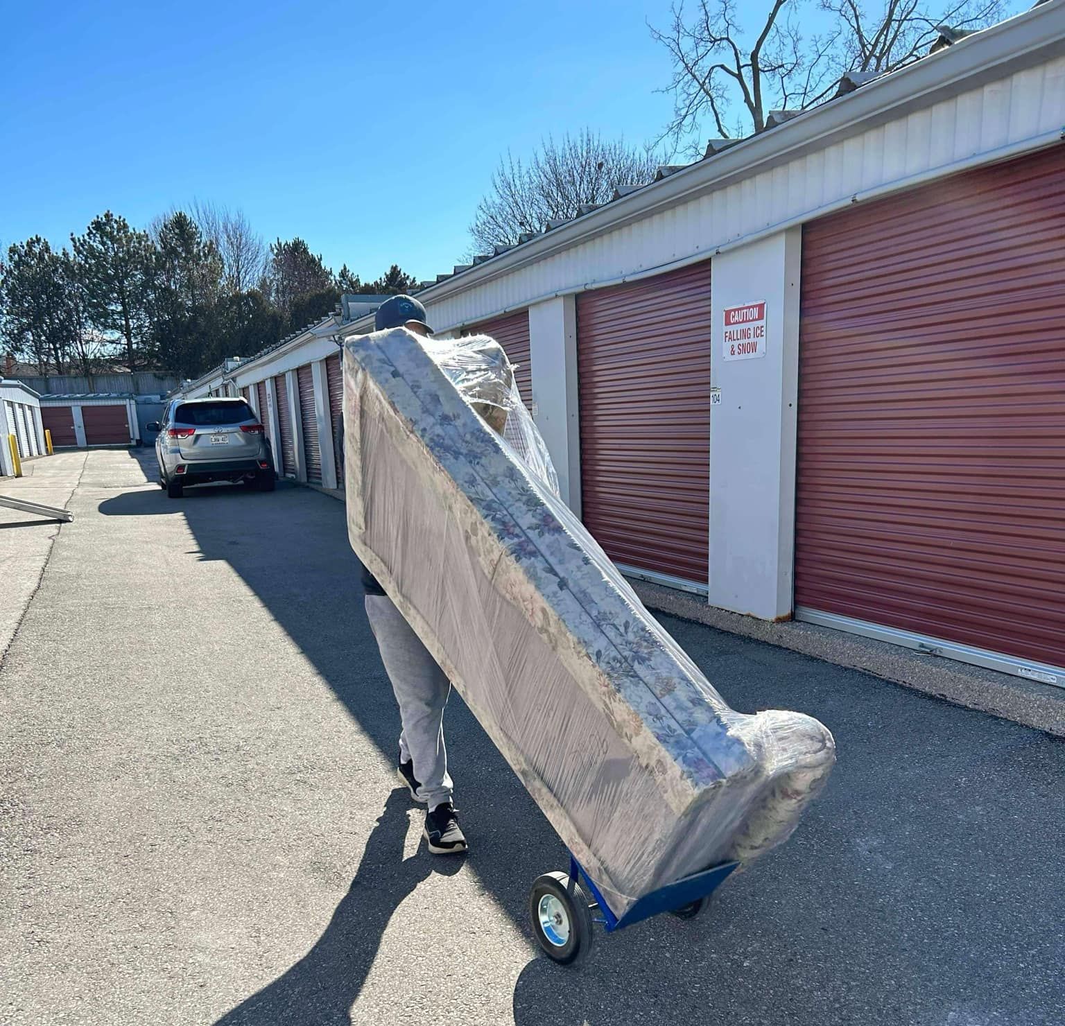 A person is pushing a mattress on a dolly in a parking lot.