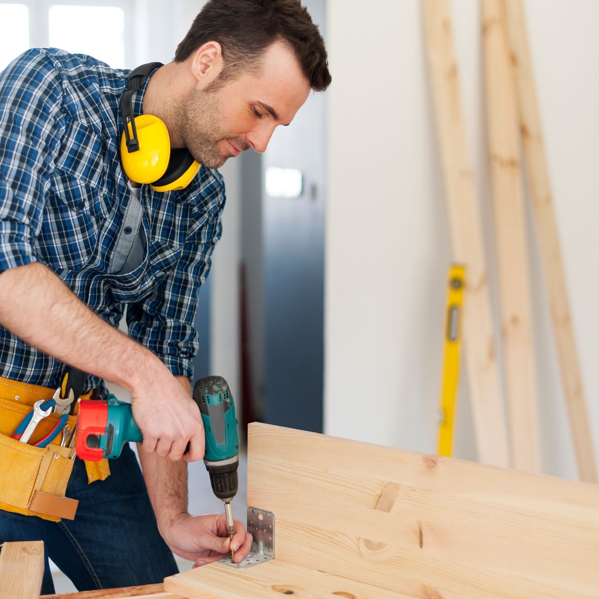 A man wearing ear protectors is using a drill on a piece of wood