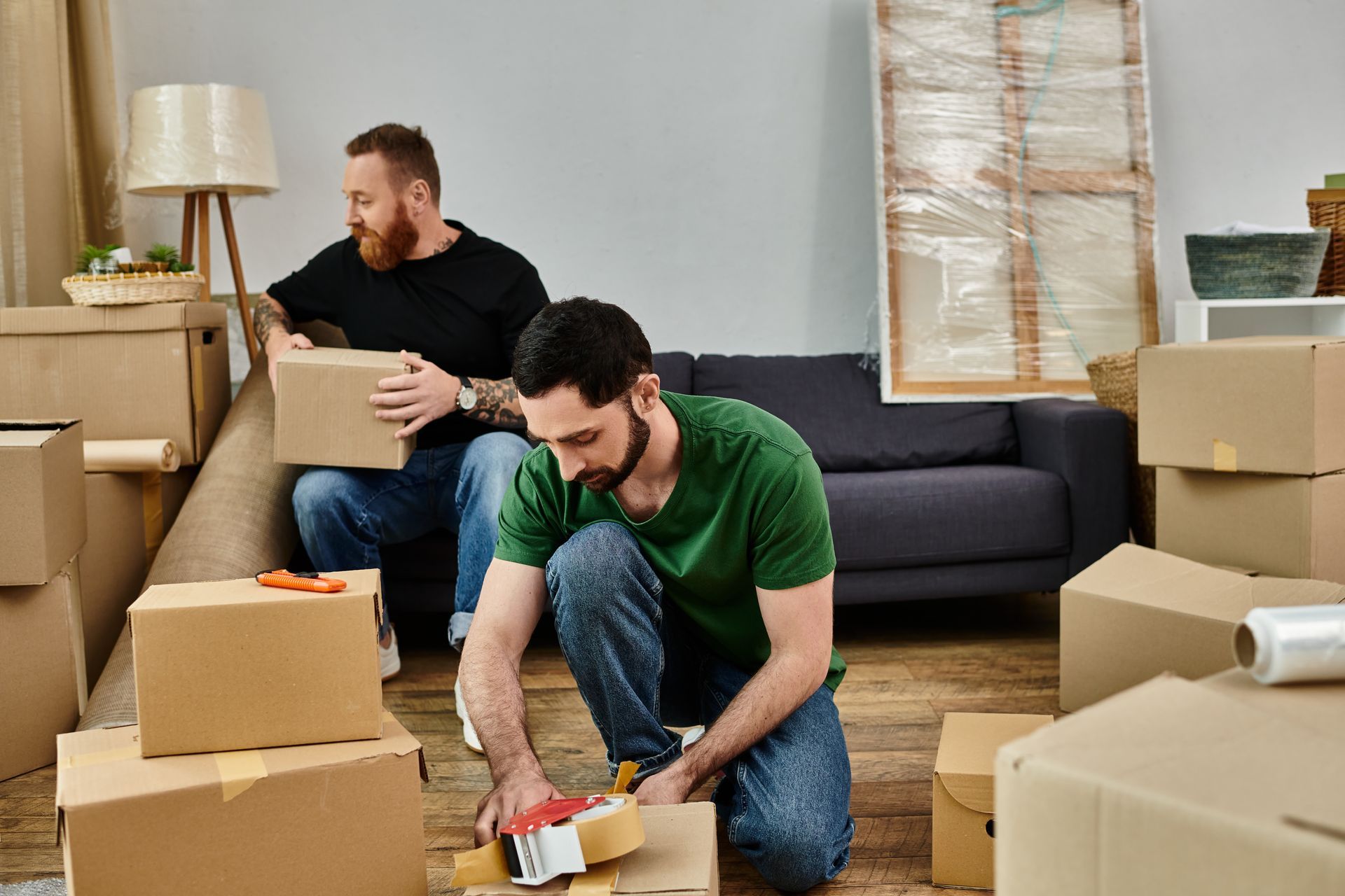 Two men are packing boxes in a living room.