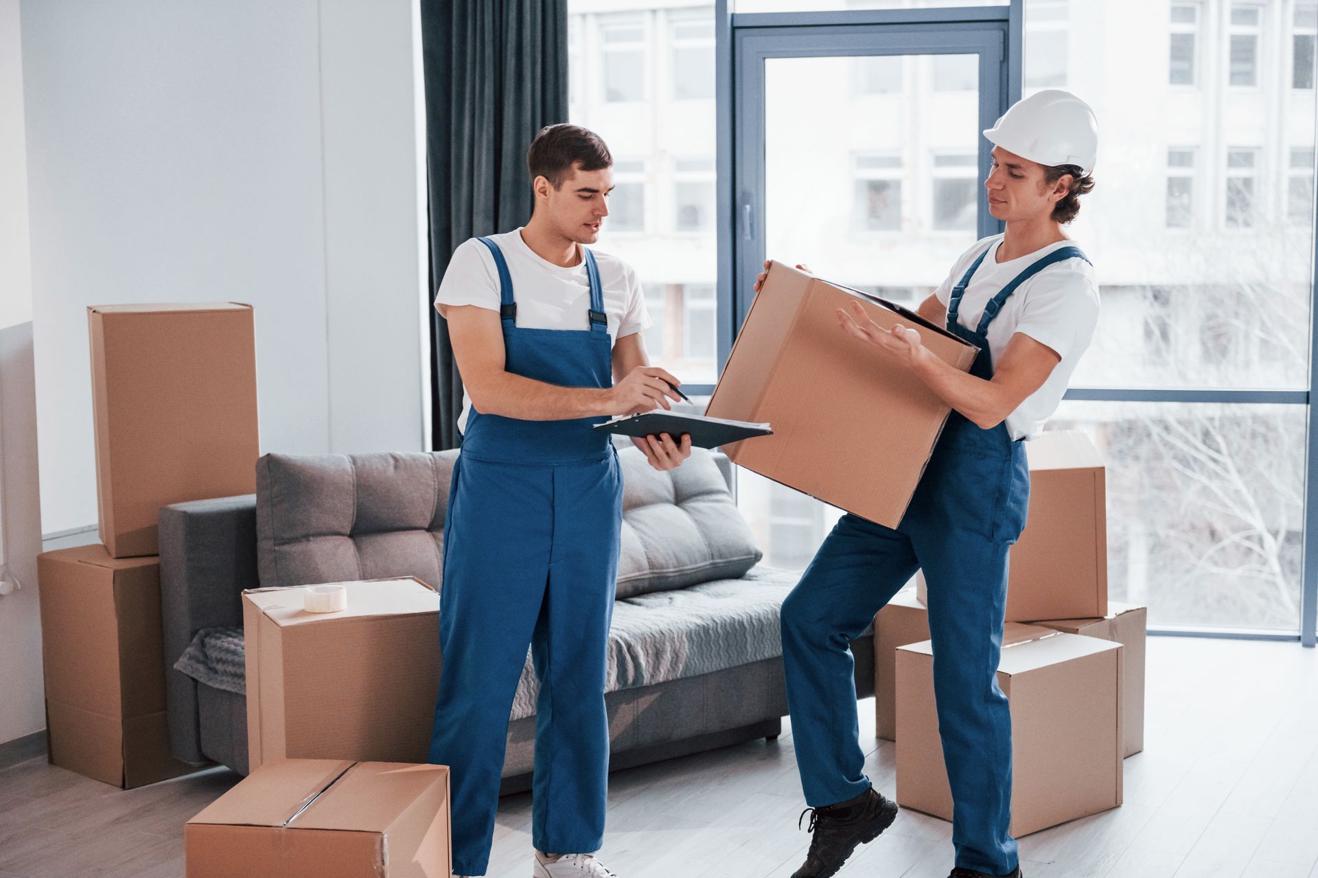 A man and a woman are moving boxes in a living room.