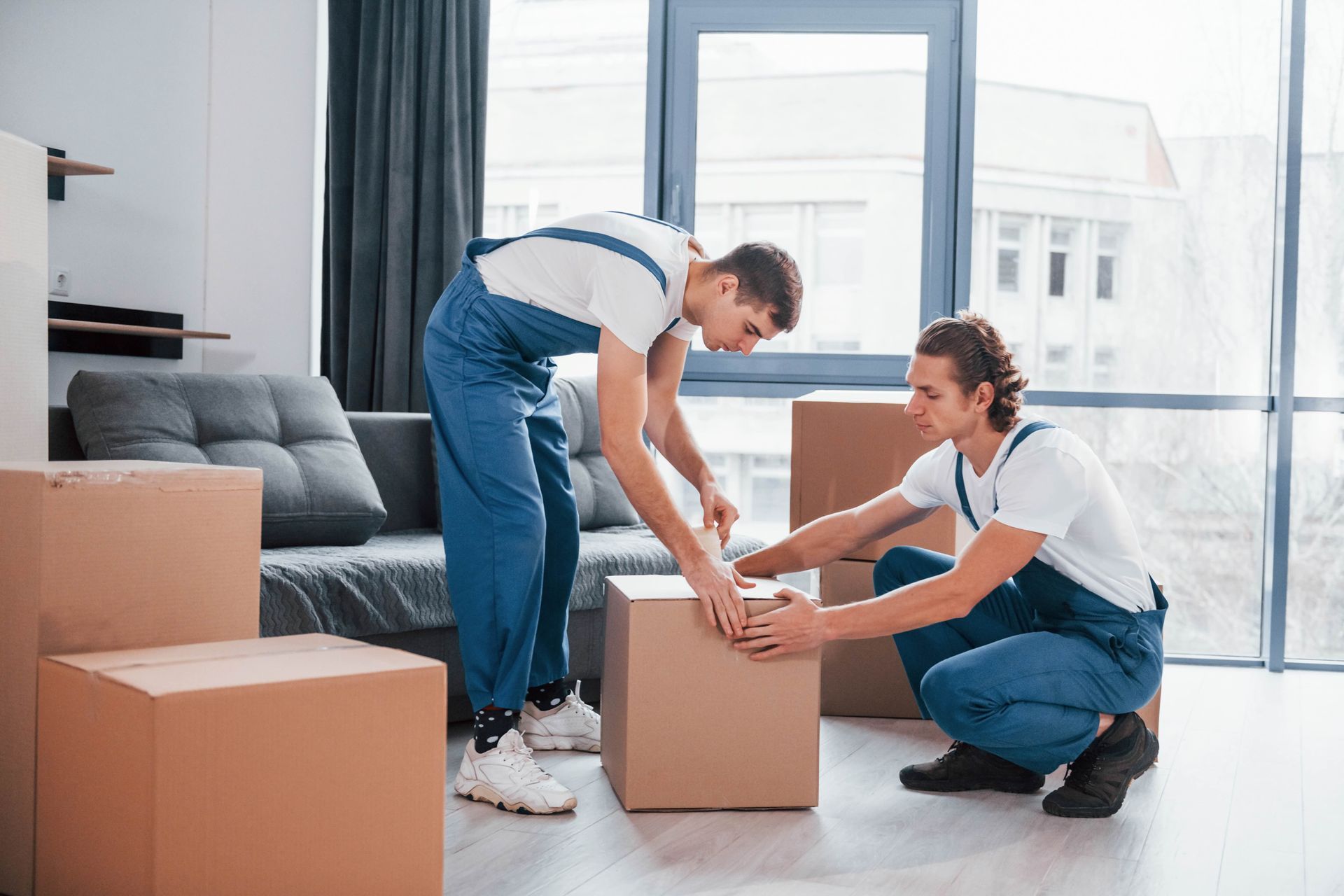 Two men are packing boxes in a living room.