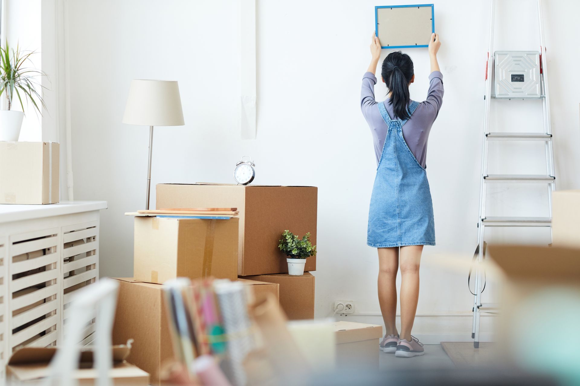 A woman is hanging a picture on a wall in a living room.