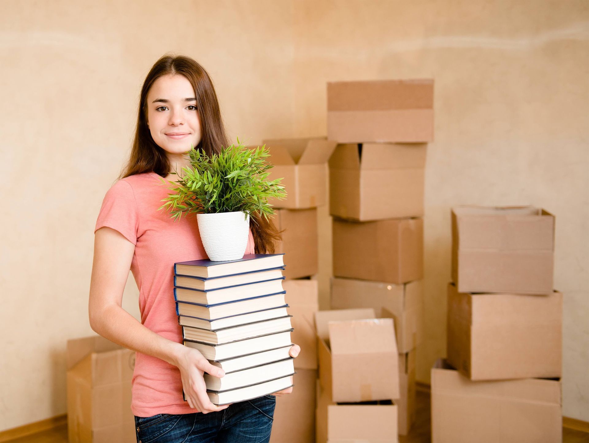 A woman is holding a stack of books and a potted plant.