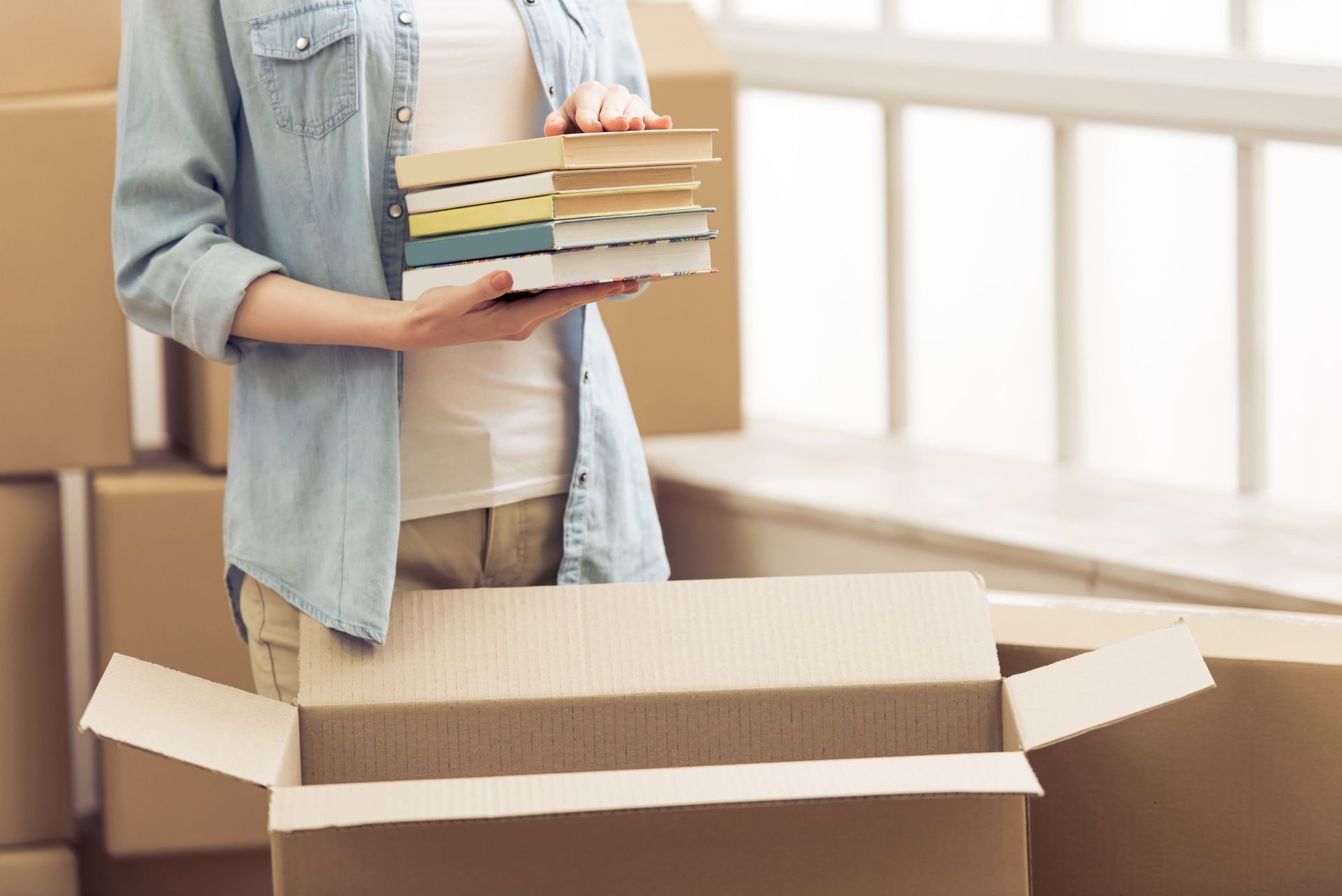 A woman is holding a stack of books and putting them in a cardboard box.