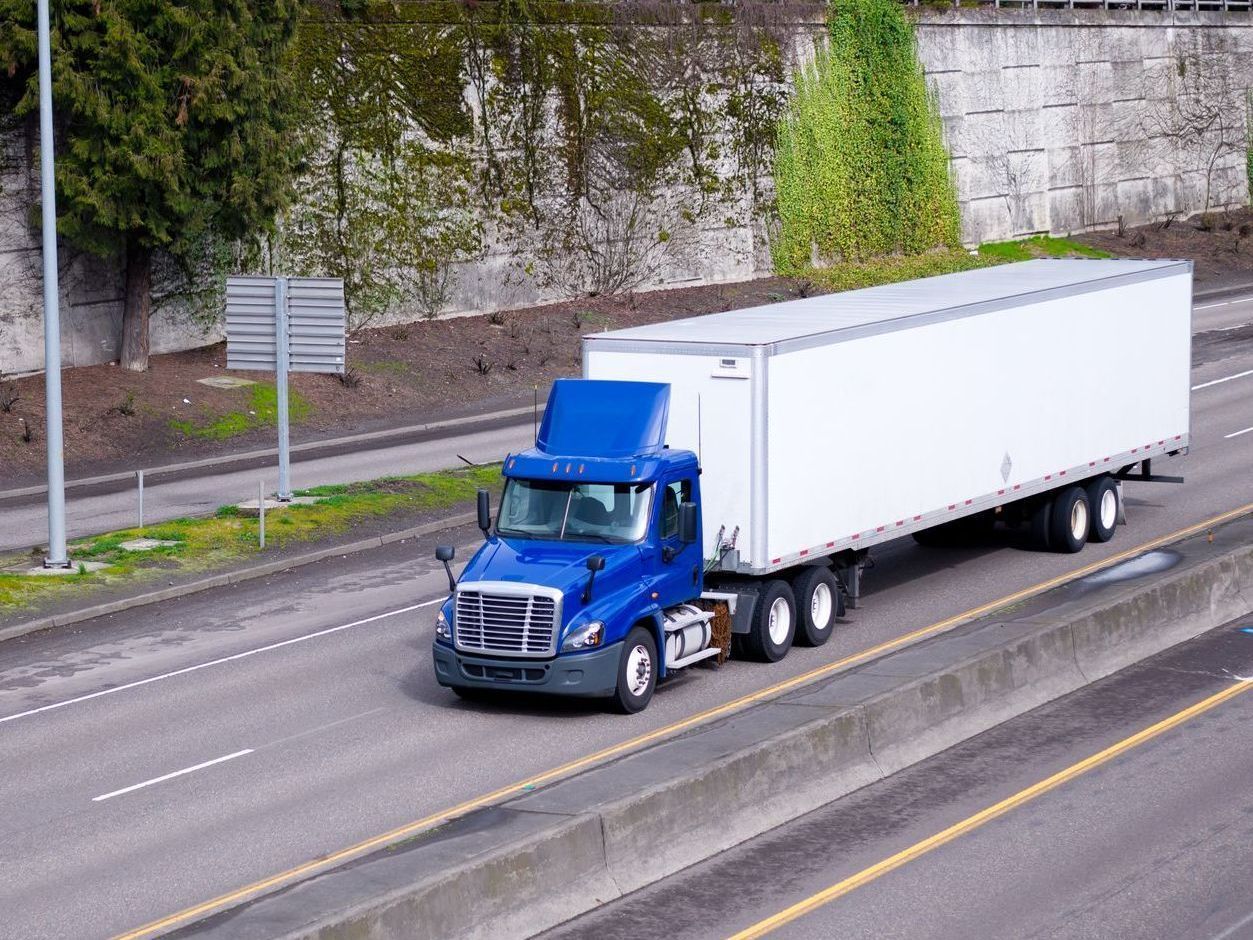 A blue semi truck with a white trailer is driving down a highway.