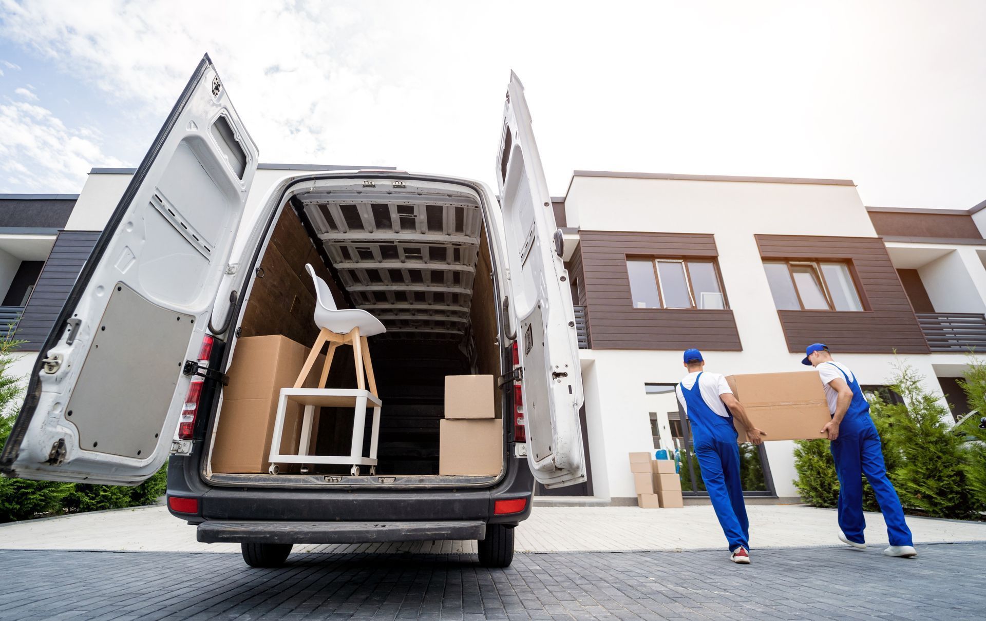 Two movers are loading boxes into a van in front of a house.