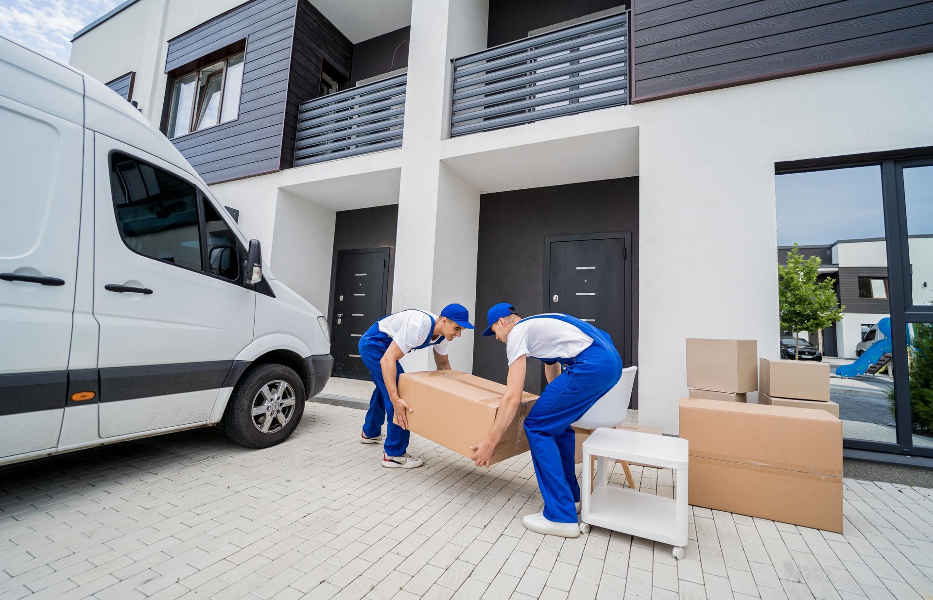 Two men are loading boxes into a van in front of a house.