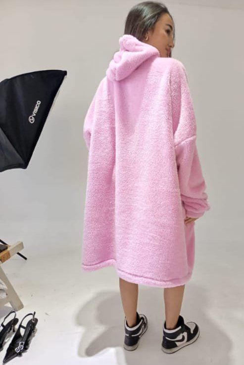 Mujer con una sudadera con capucha de sherpa rosa de gran tamaño y zapatillas blancas y negras, de pie en un estudio.