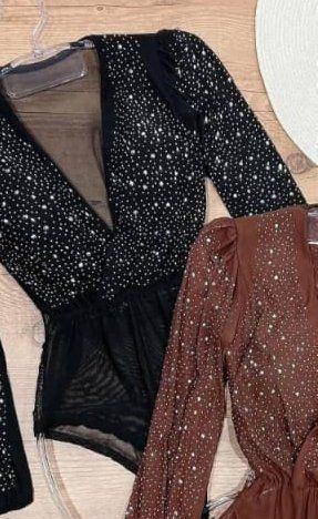 Bodys negros y marrones con detalles brillantes, colgados en perchas.