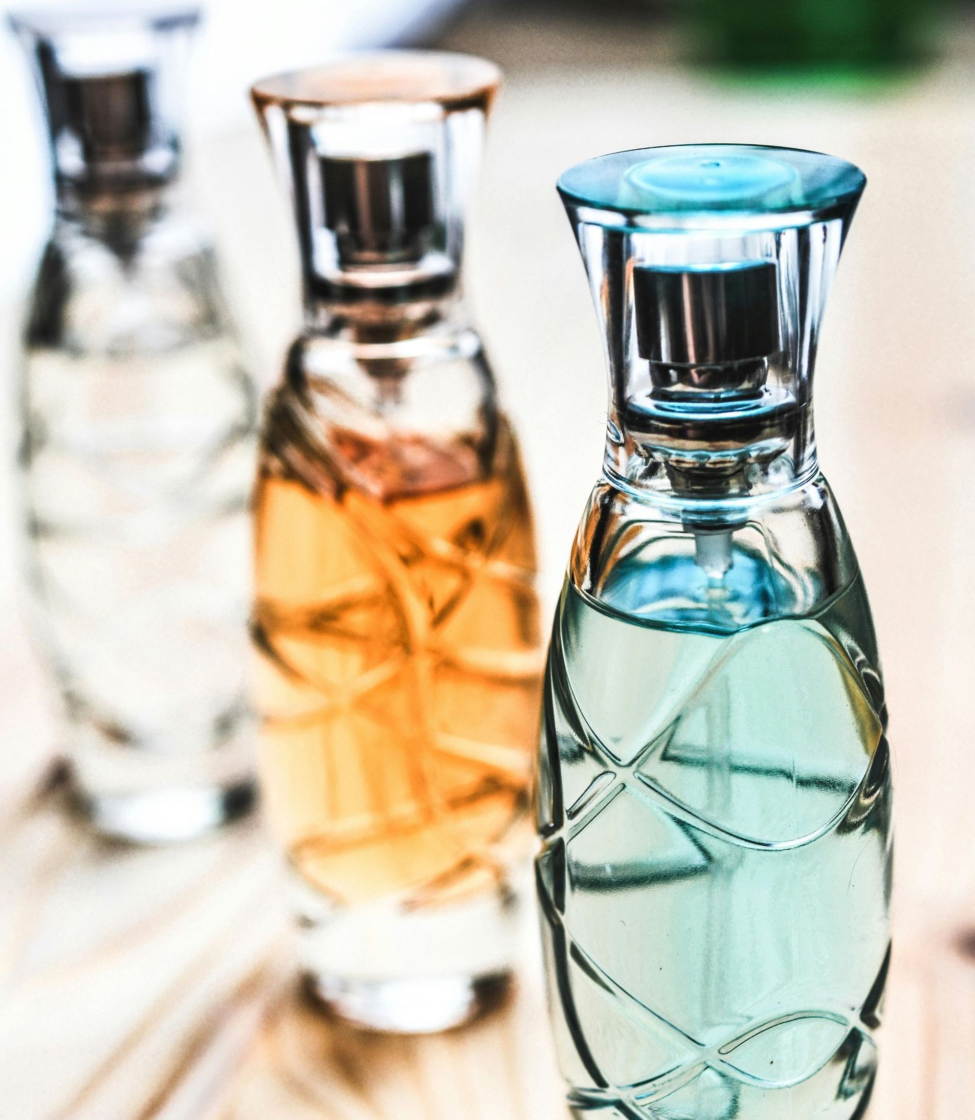 Tres frascos de perfume, de distintos colores: transparente, ámbar y azul, en fila, sobre una superficie de madera clara.