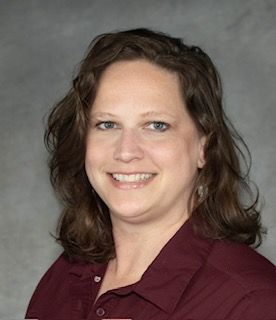 A woman in a maroon shirt is smiling for the camera.