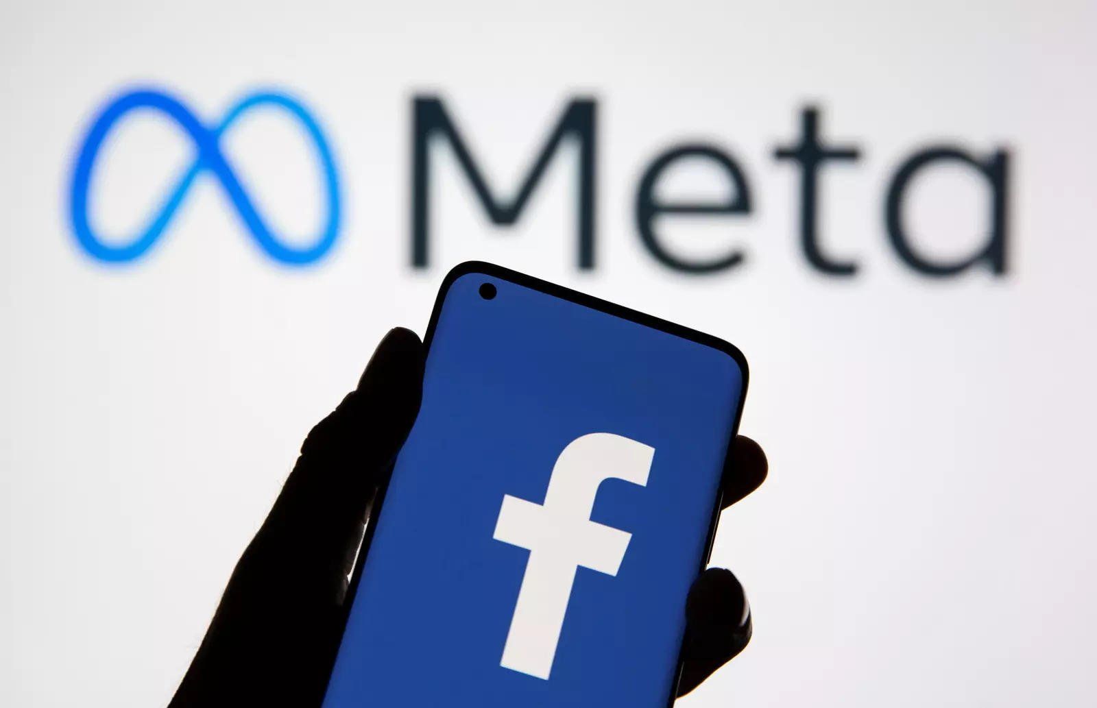A person is holding a cell phone in front of a facebook logo.