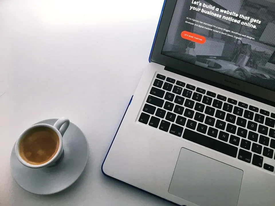 A laptop computer is open on a table next to a cup of coffee.