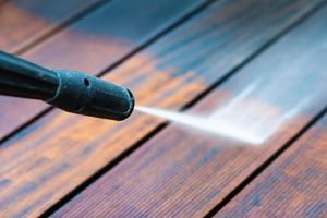 A person is using a high pressure washer to clean a wooden deck.