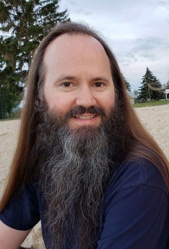 Shawn Aller with long hair and a beard is sitting on the beach.