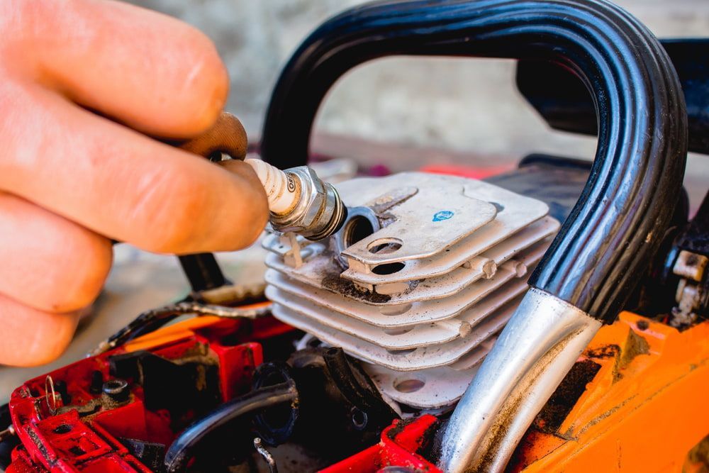 A Person Is Putting A Spark Plug Into A Chainsaw Engine — Rocky Small Motor Service In Rockhampton, QLD