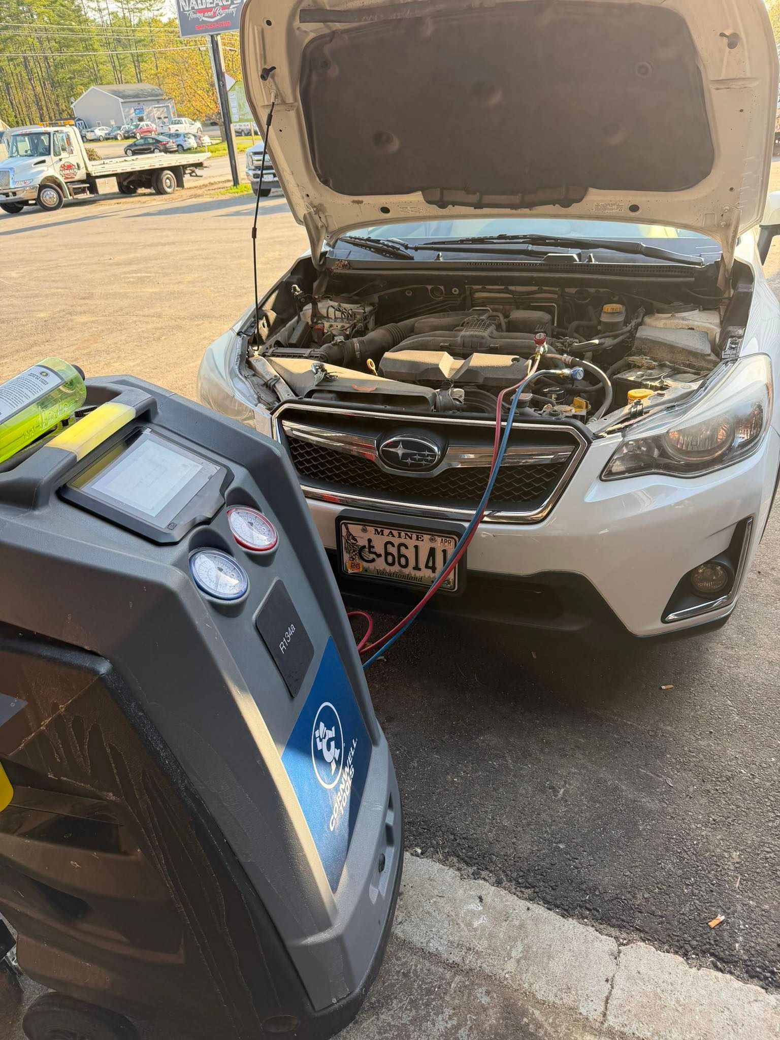 Car with hood open and jumper cables connected to a portable jump starter in a parking lot