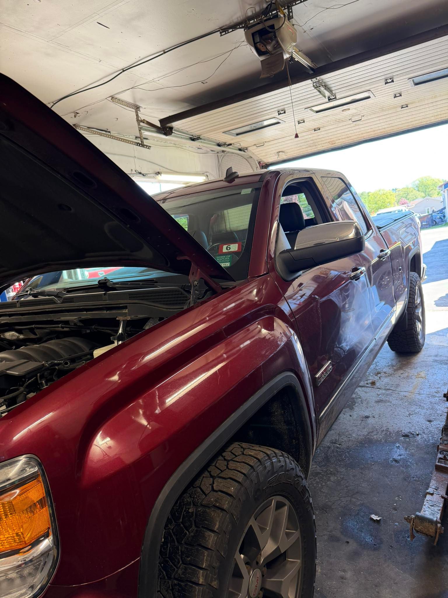 Maroon pickup truck parked inside a garage with its hood open and engine exposed.