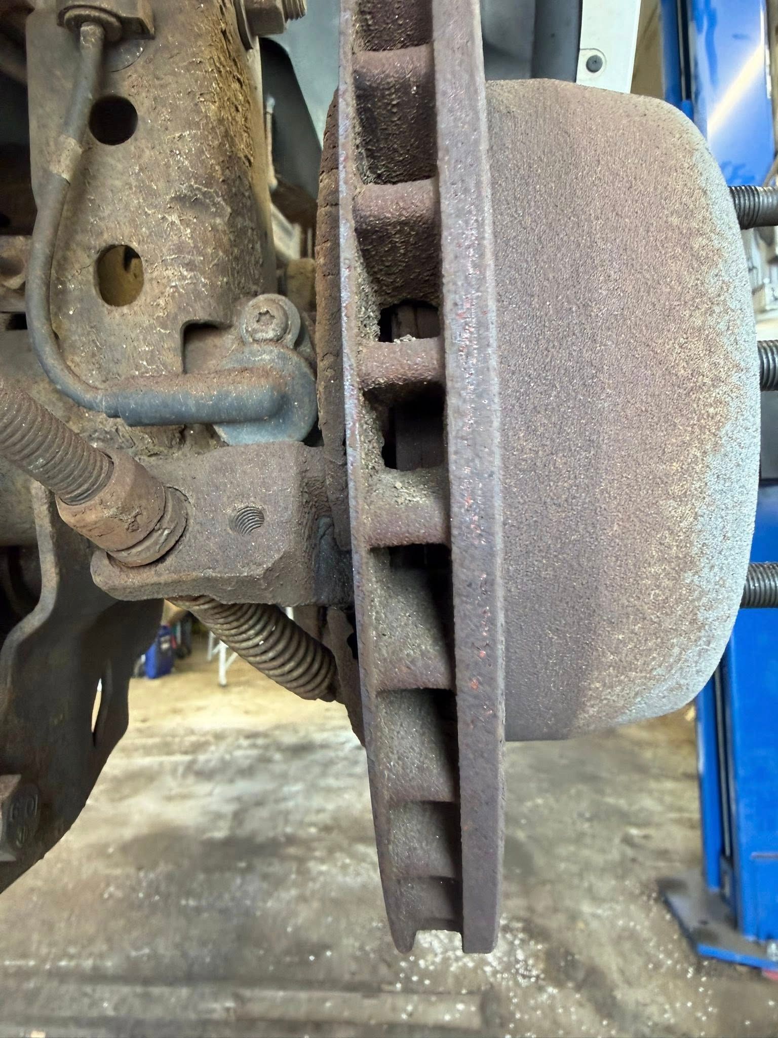 Close-up of a car brake rotor and caliper with wheel removed in a garage.