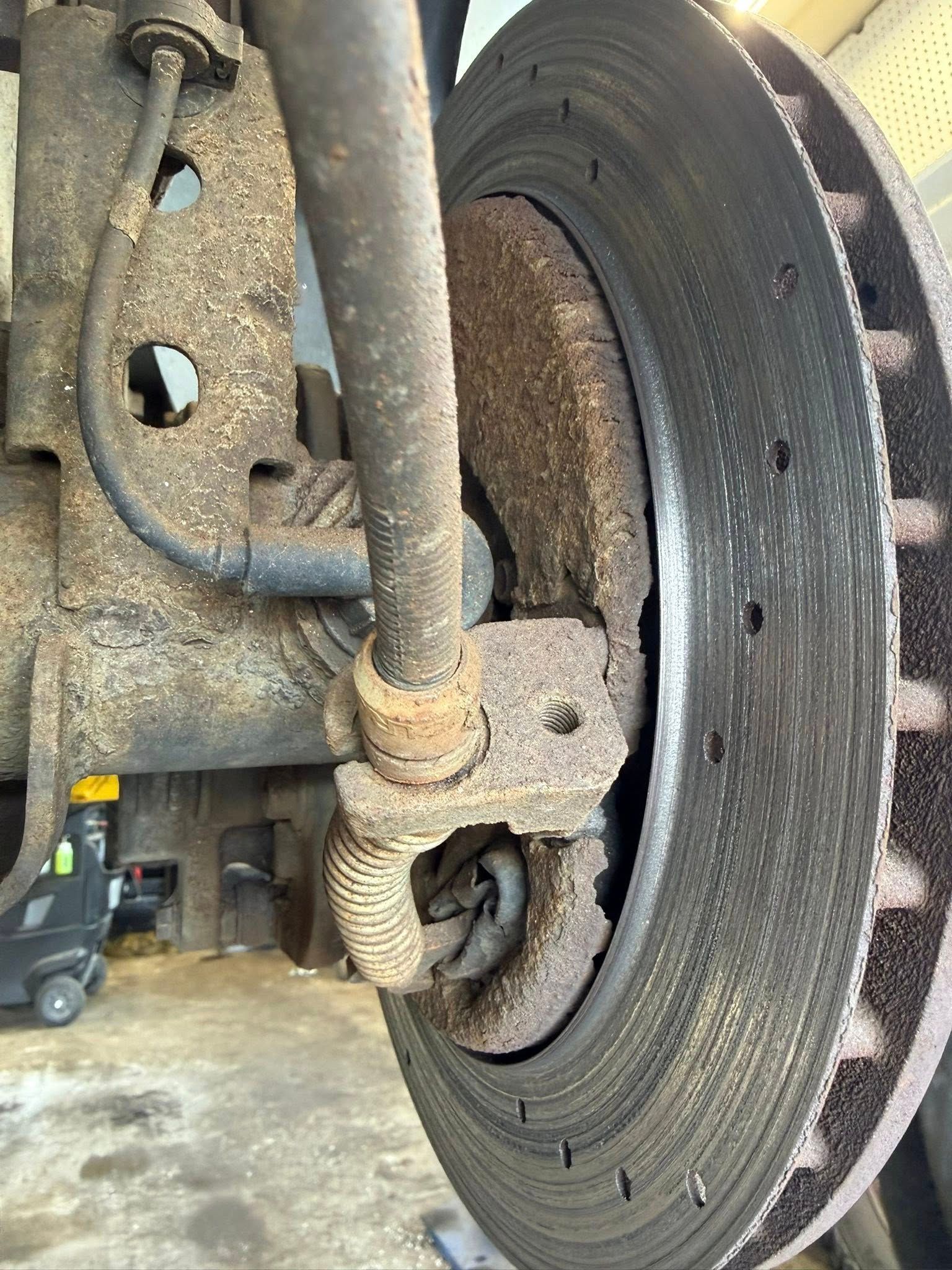 Close-up of a dusty car brake rotor and suspension components in a garage.