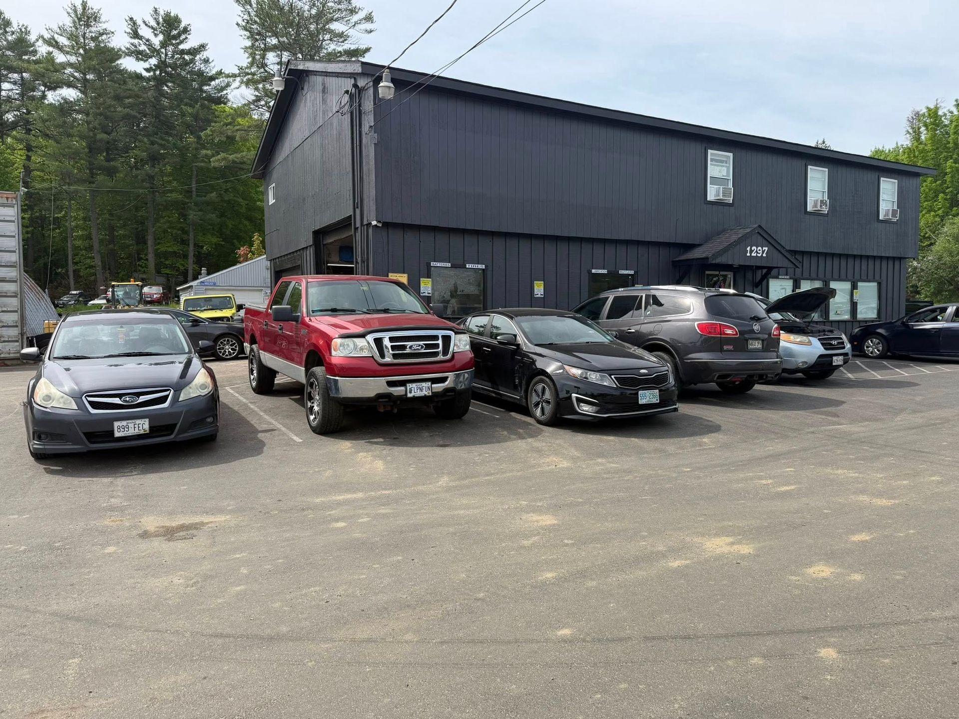Parking lot with several parked cars in front of a dark two-story building.