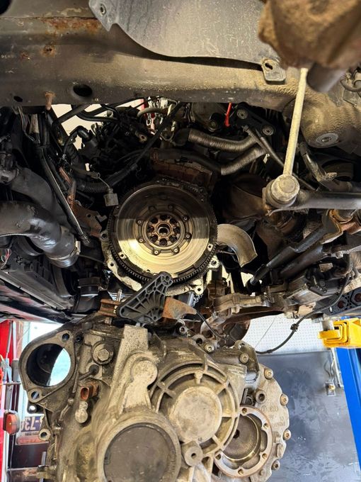 Undercarriage of a vehicle in a workshop, with the transmission and drivetrain removed and parts lying below.