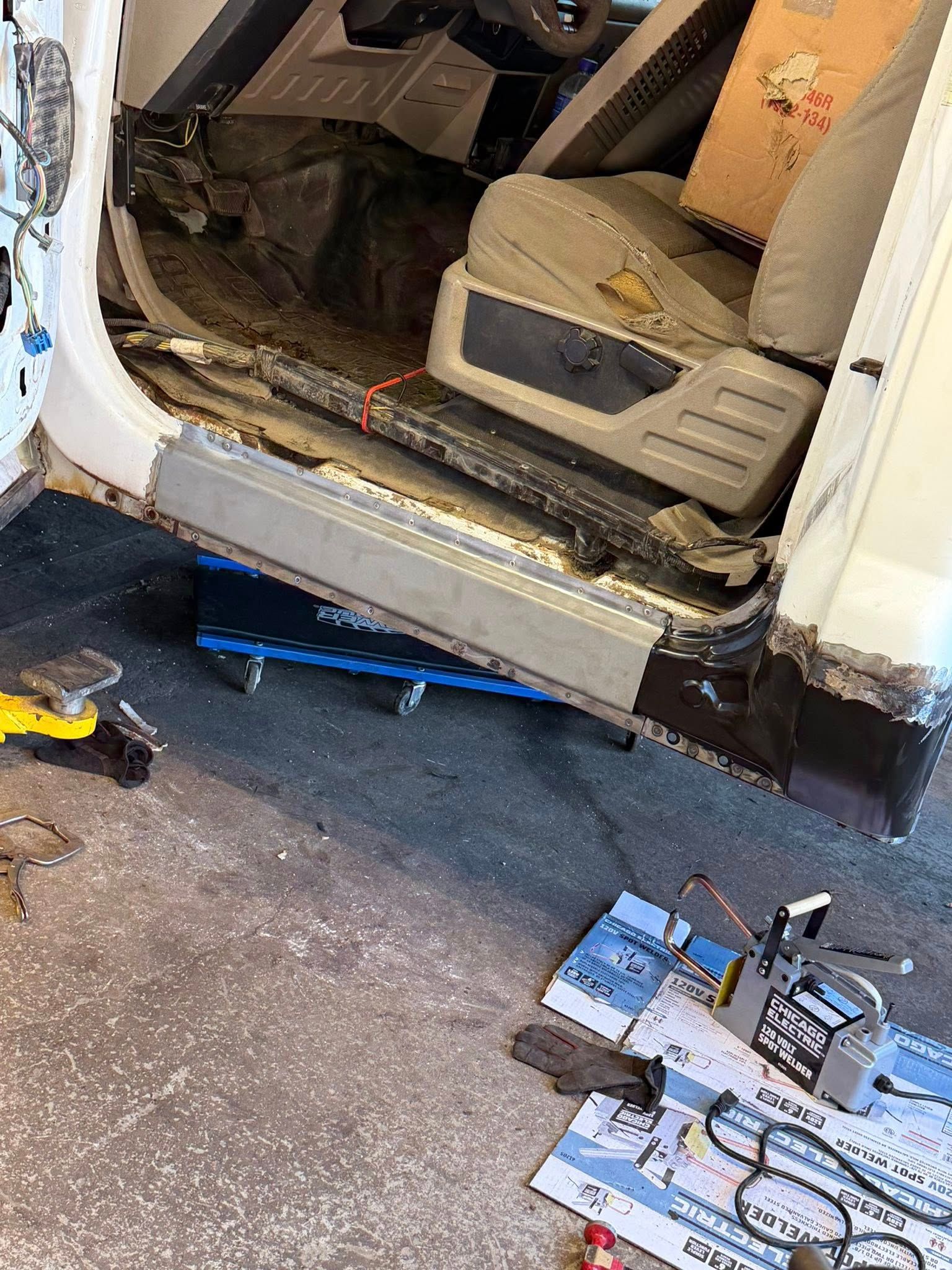 Damaged white van with exposed interior, tools on the ground outside a garage-like space