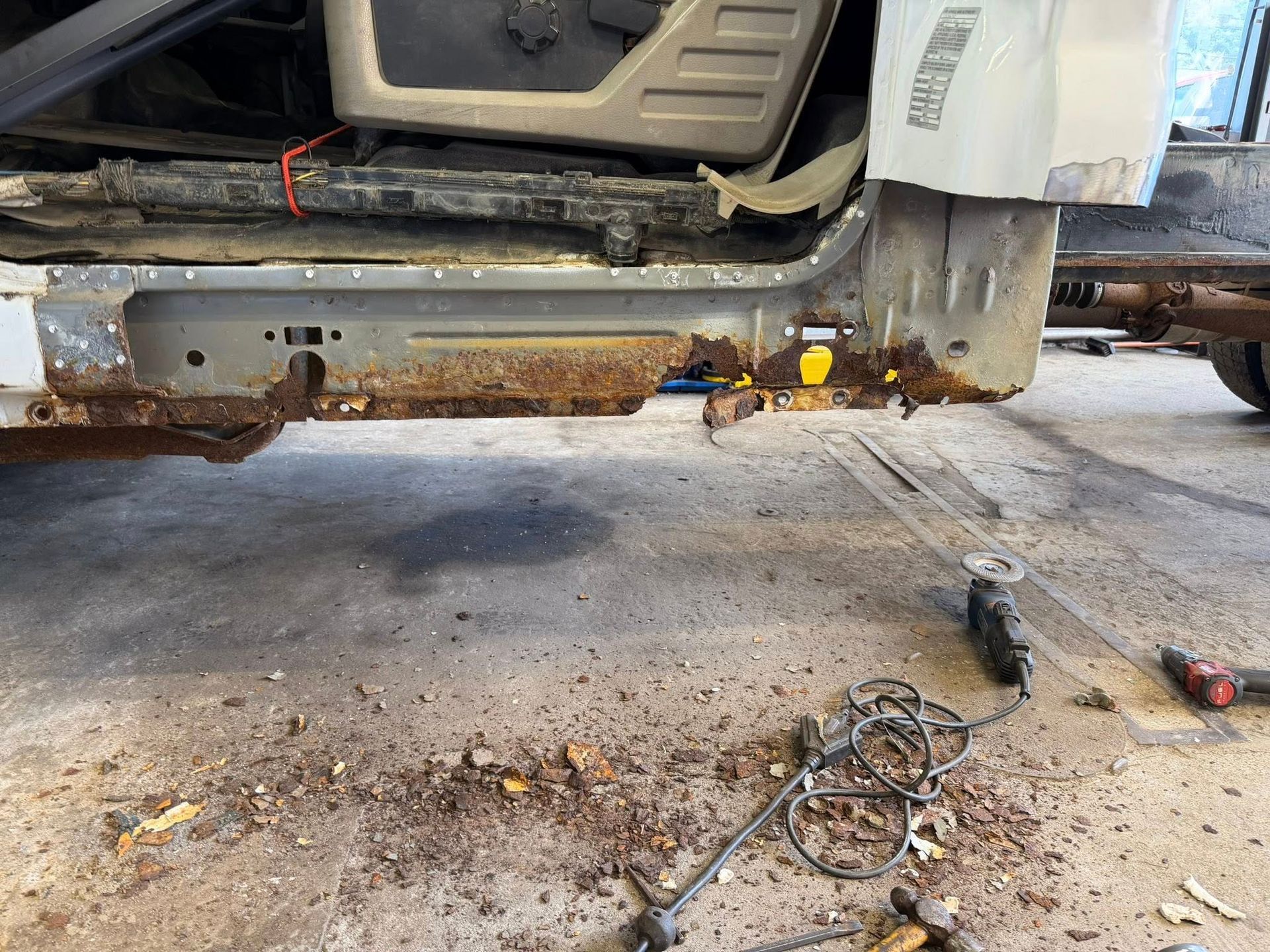 Rusty vehicle undercarriage with tools on the ground in a repair shop
