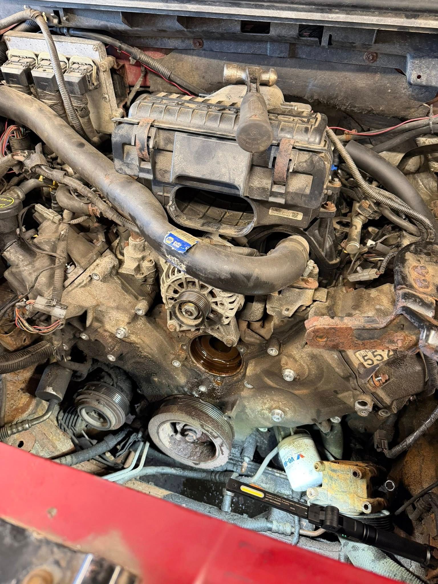 Dirty car engine bay with exposed components and heavy rust or oil grime