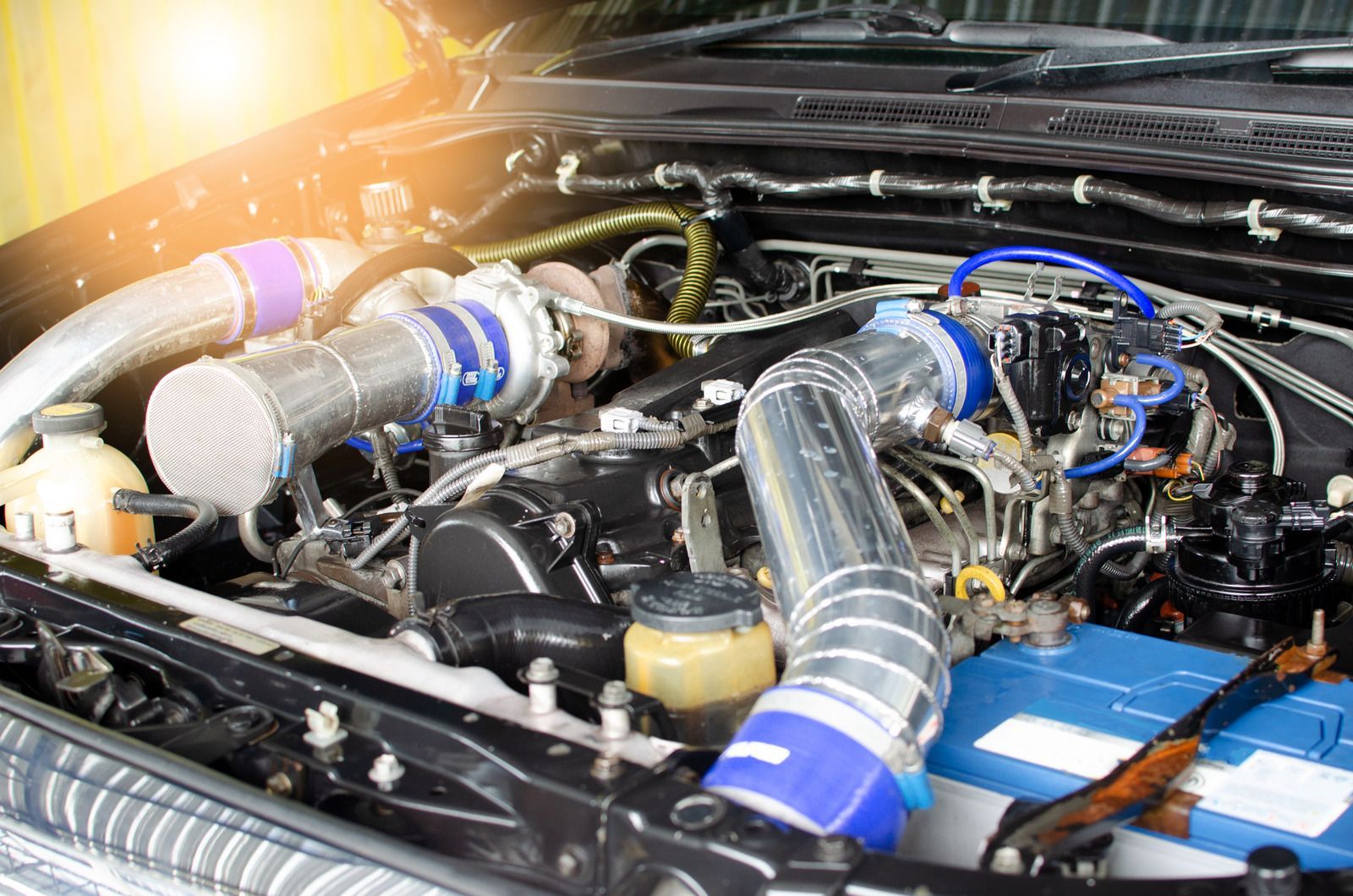 Car engine bay with twin silver turbo piping and blue hoses under the hood