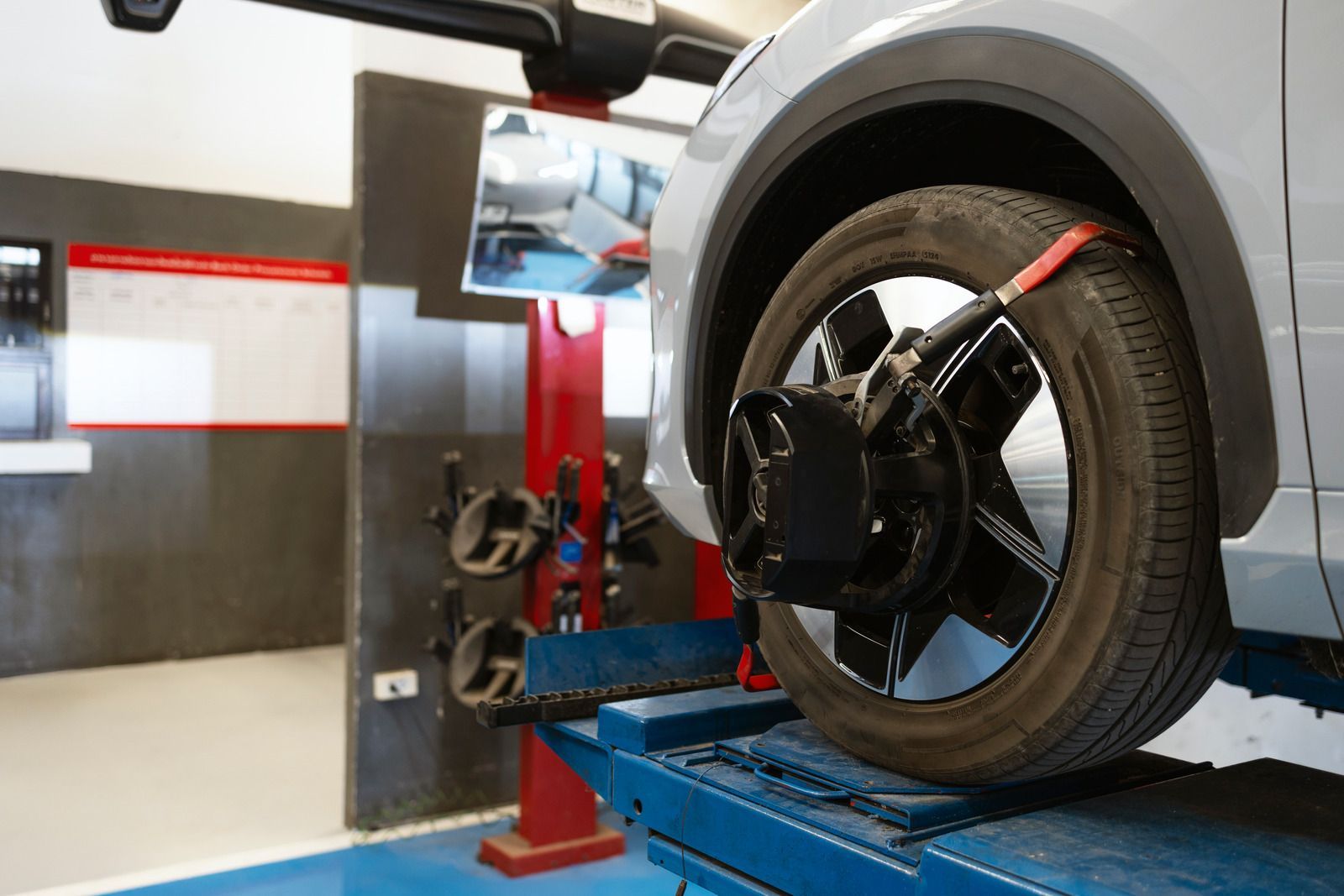 Car in a garage on a blue lift, with a wheel alignment machine attached to the front wheel.