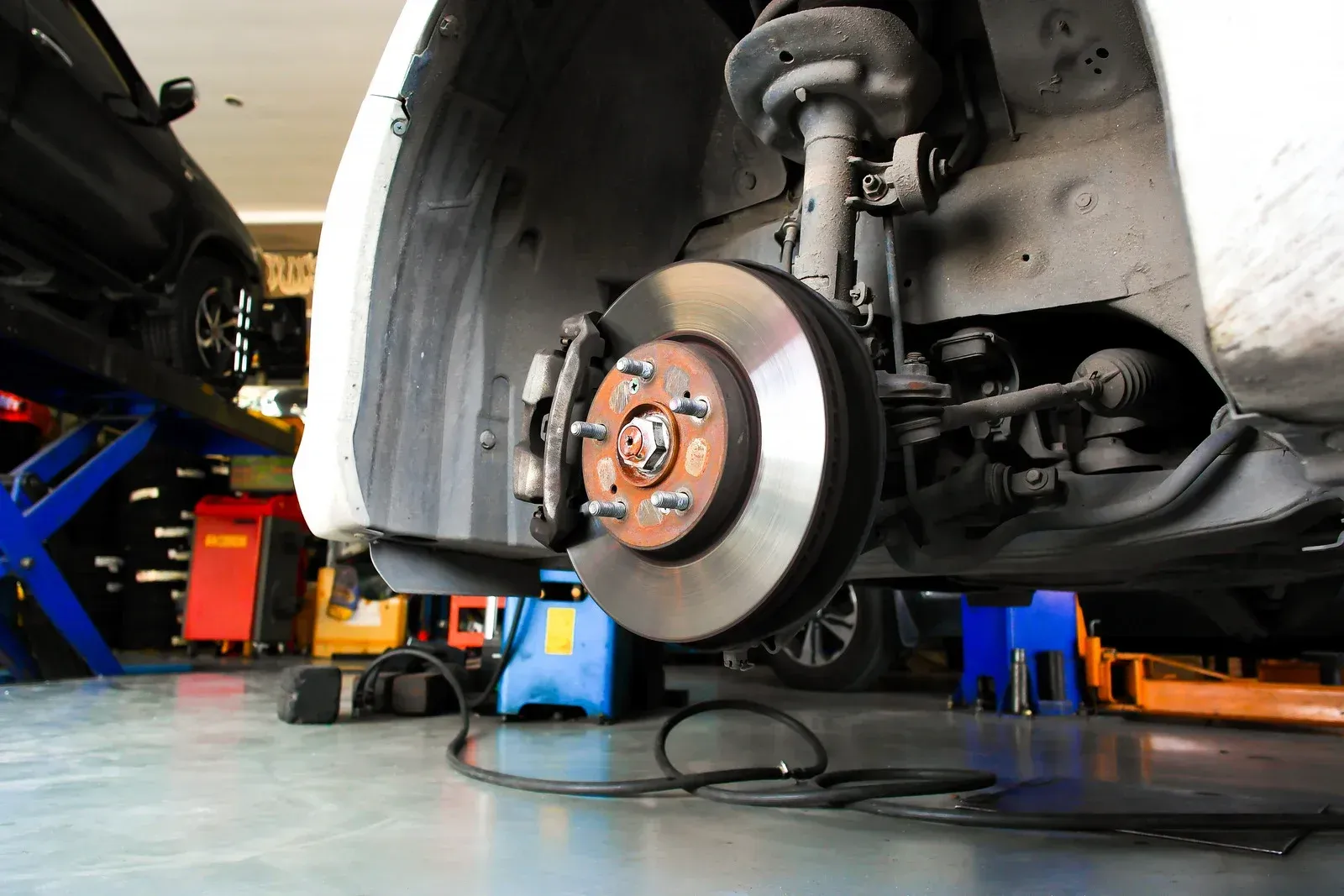 Car on a lift with front wheel removed, showing brake rotor and suspension in an auto repair shop