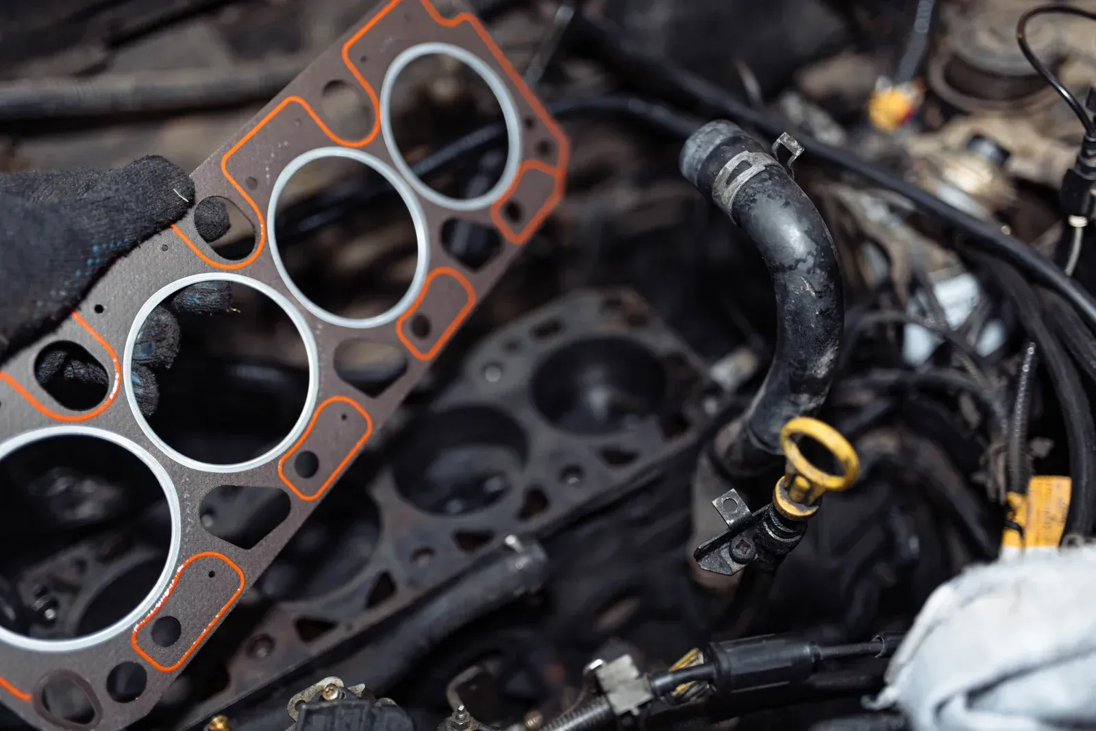Close-up of a car engine block with a gasket and yellow oil dipstick in a greasy repair setting