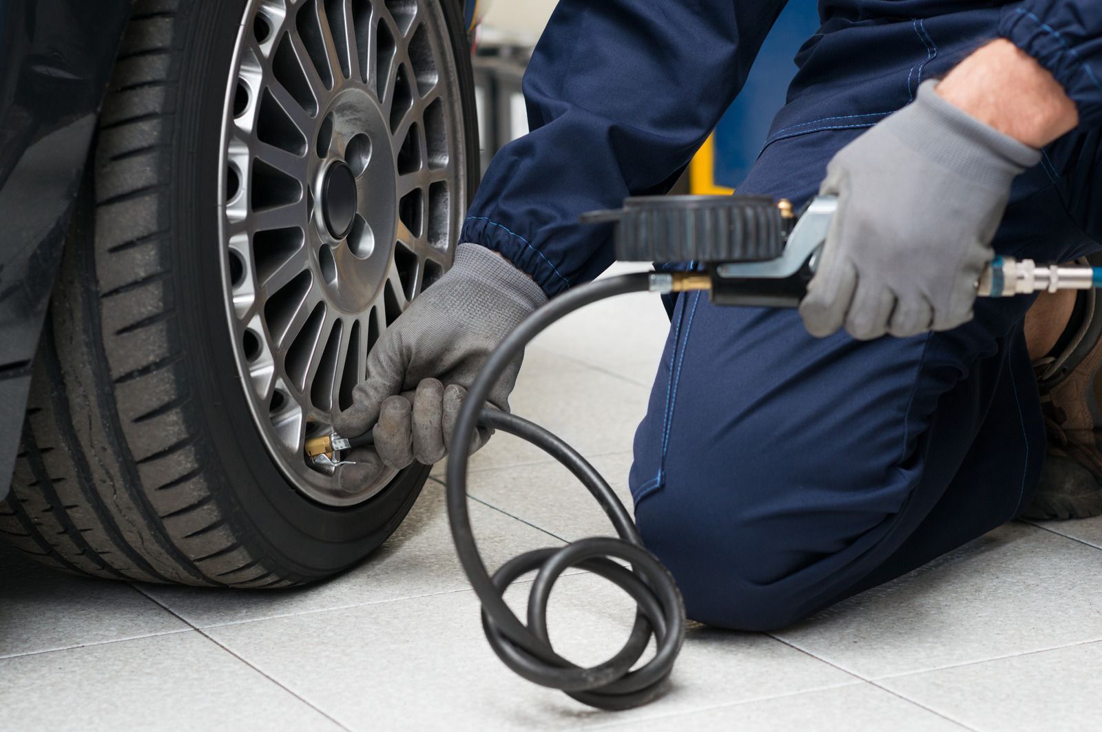 Mechanic inflating a car tire with a handheld air pump while kneeling beside the wheel