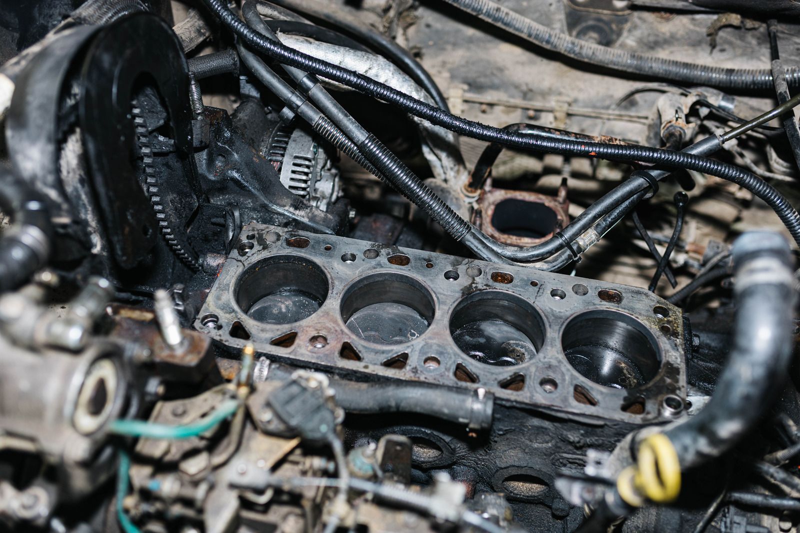 Disassembled engine block with cylinder openings and tangled wiring, covered in grime and oil.