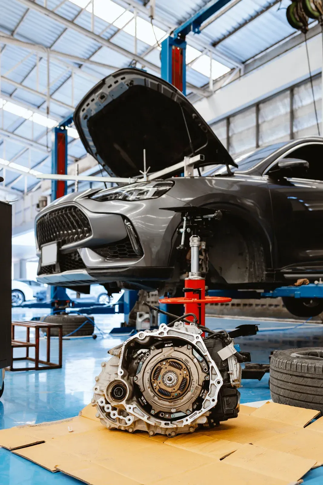 Car in auto shop with hood open, raised on a lift, engine removed on the floor.