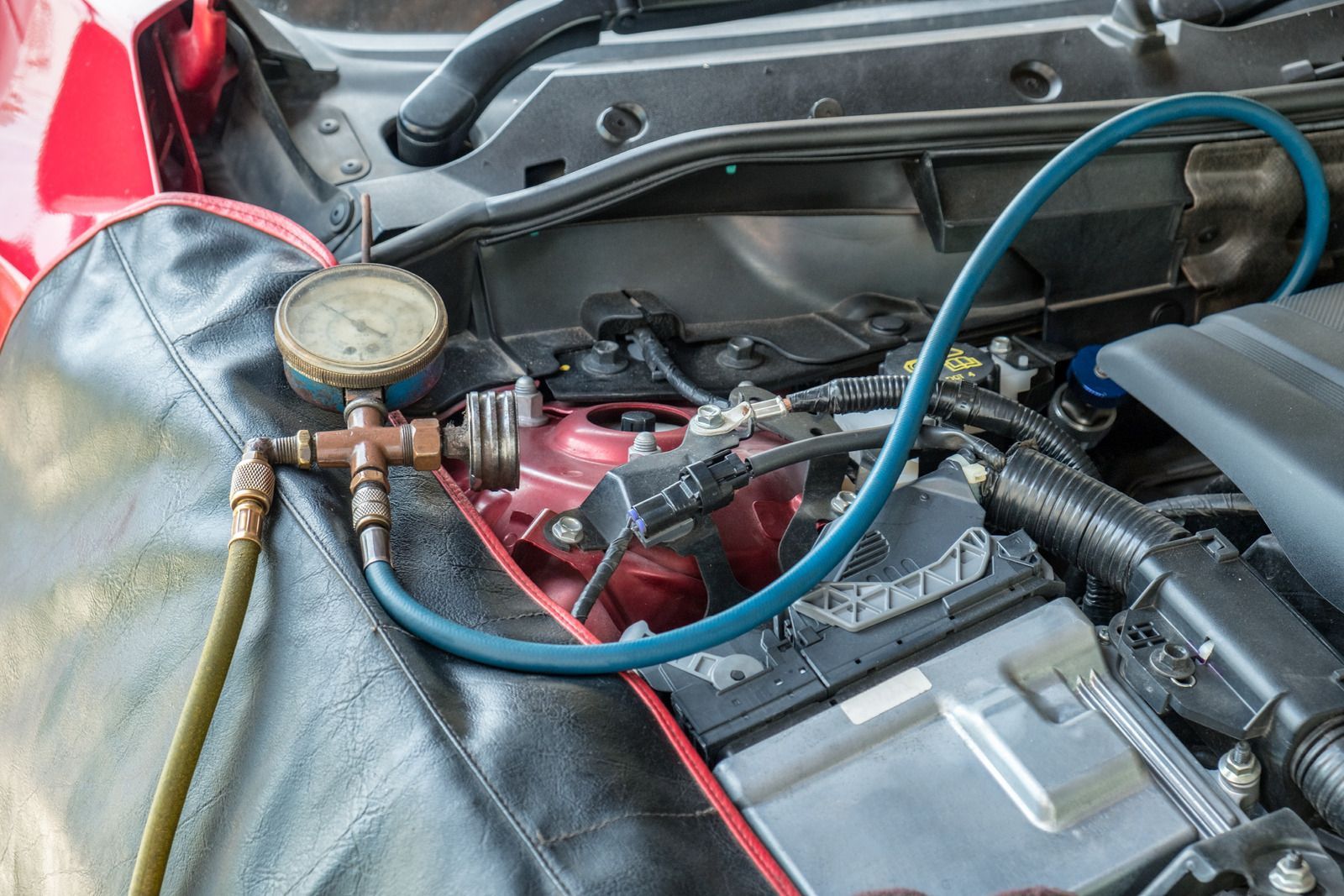 Car engine bay with an AC gauge set and blue hose connected to the system