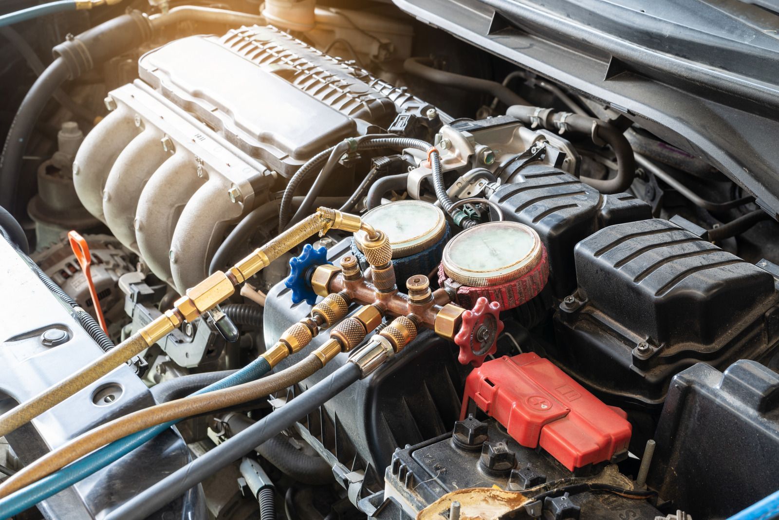 Car engine bay with open hood, showing hoses, filters, and red battery terminal connections