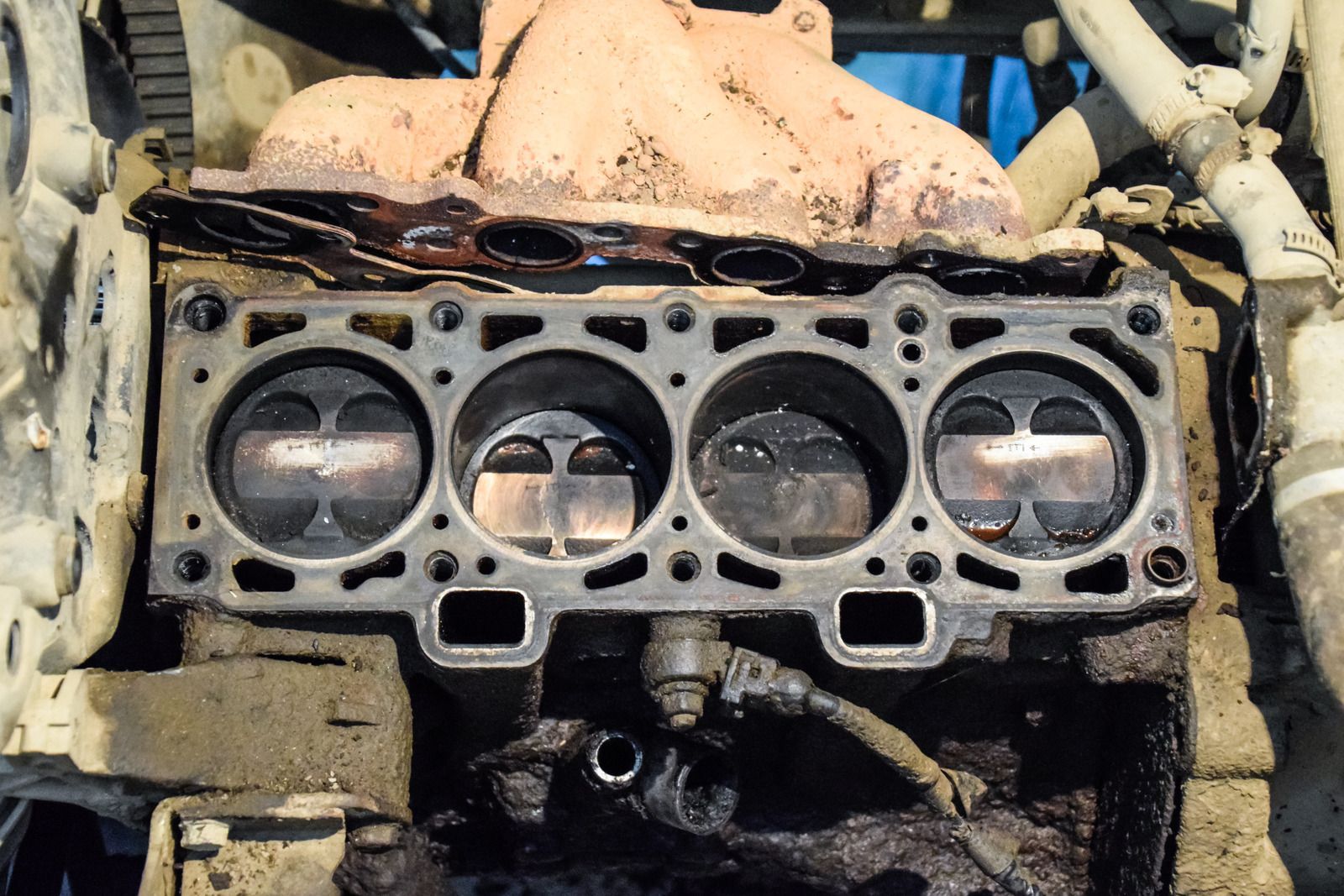 Mechanic using tools to service a car engine under the hood, with a coolant reservoir visible.