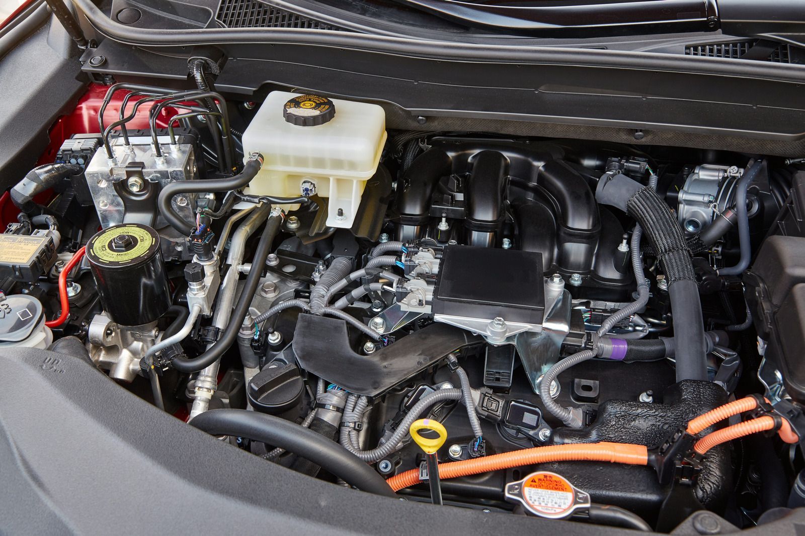 Car engine bay with exposed components, hoses, and orange cable in a compact compartment