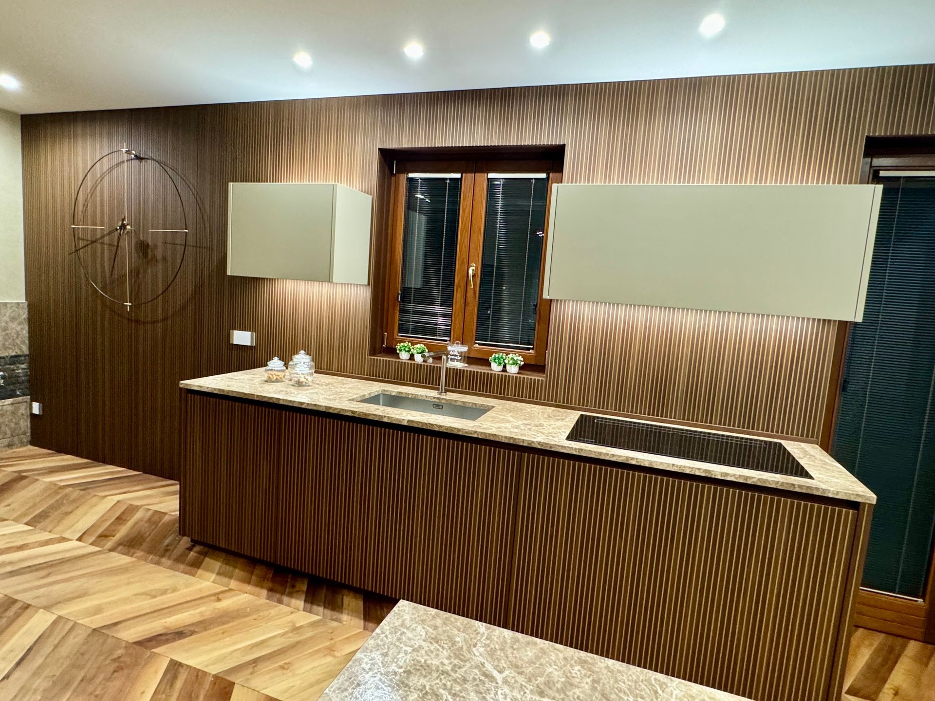 Una cucina con mobili in legno, ripiani in granito, un lavandino e un orologio a parete.