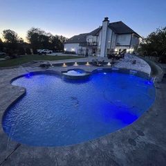 A large swimming pool is lit up at night in front of a large house.